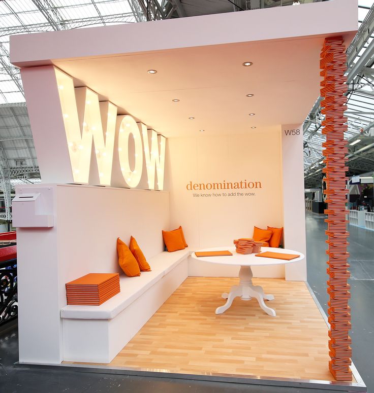 an exhibition booth with orange and white pillows on the bench, in front of a sign that says wow