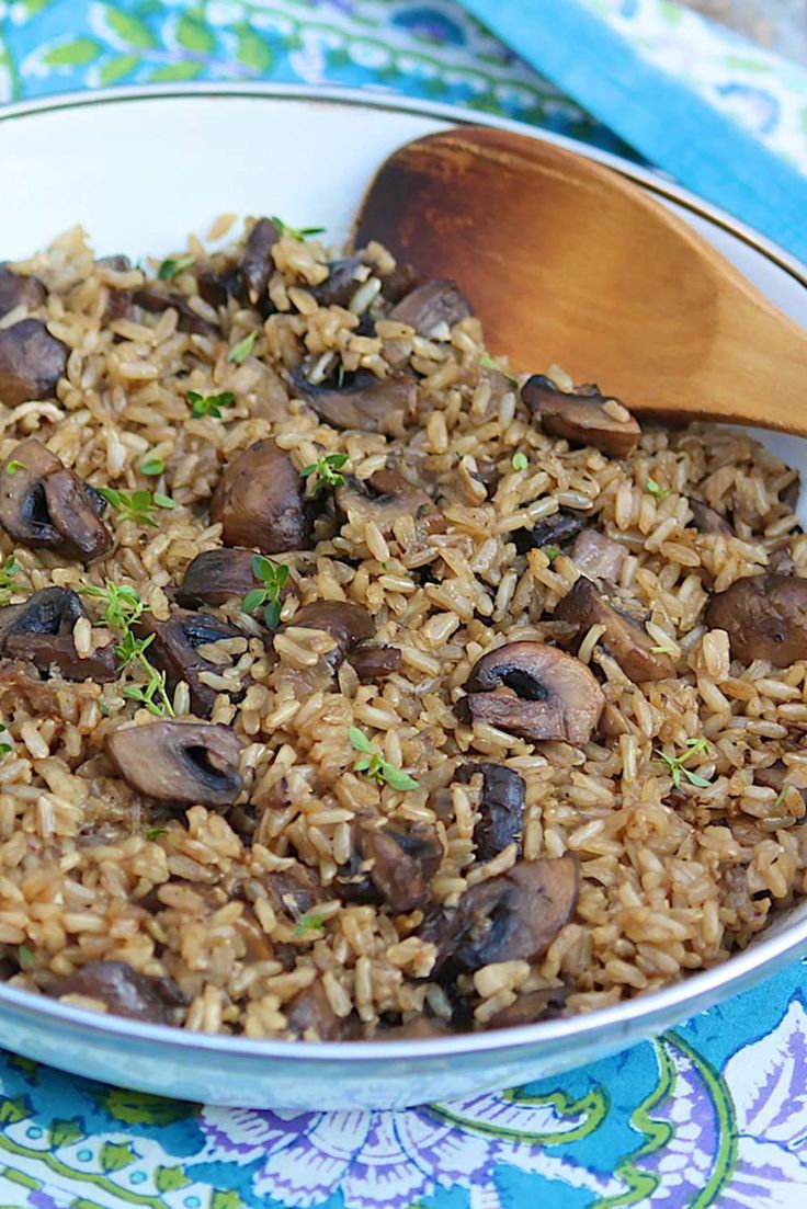 a bowl filled with rice and mushrooms on top of a blue table cloth next to a wooden spoon