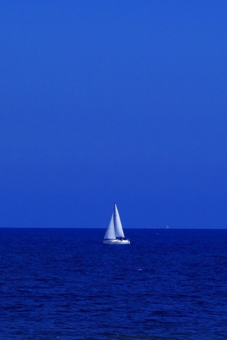 a sailboat is out on the open blue water in front of a bright blue sky