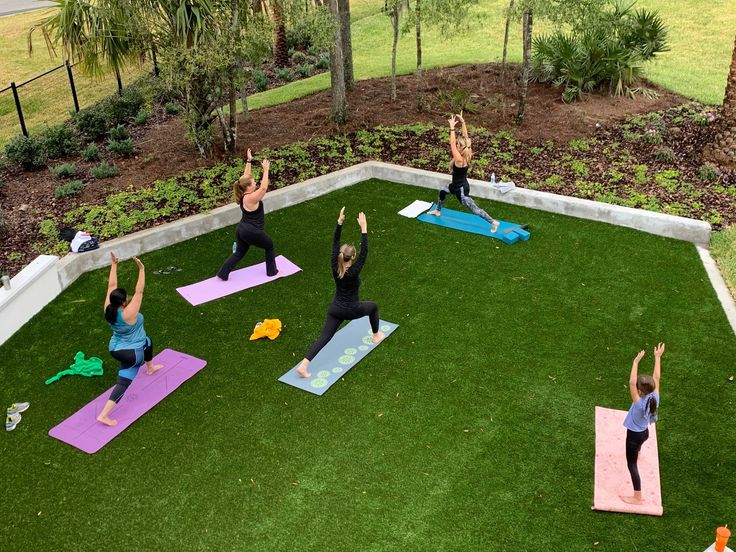 a group of people doing yoga on mats in a yard with artificial grass and trees