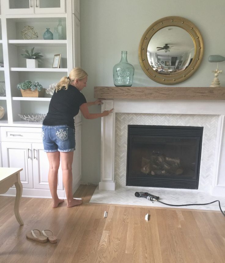 a woman standing in front of a fireplace with a mirror on the wall above it