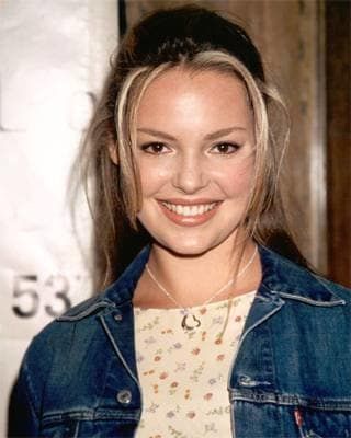 a young woman wearing a denim jacket and smiling at the camera with her hair in a bun