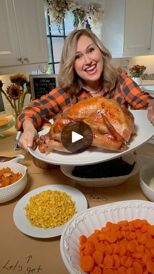 a woman holding a turkey on a platter surrounded by other plates and bowls full of food