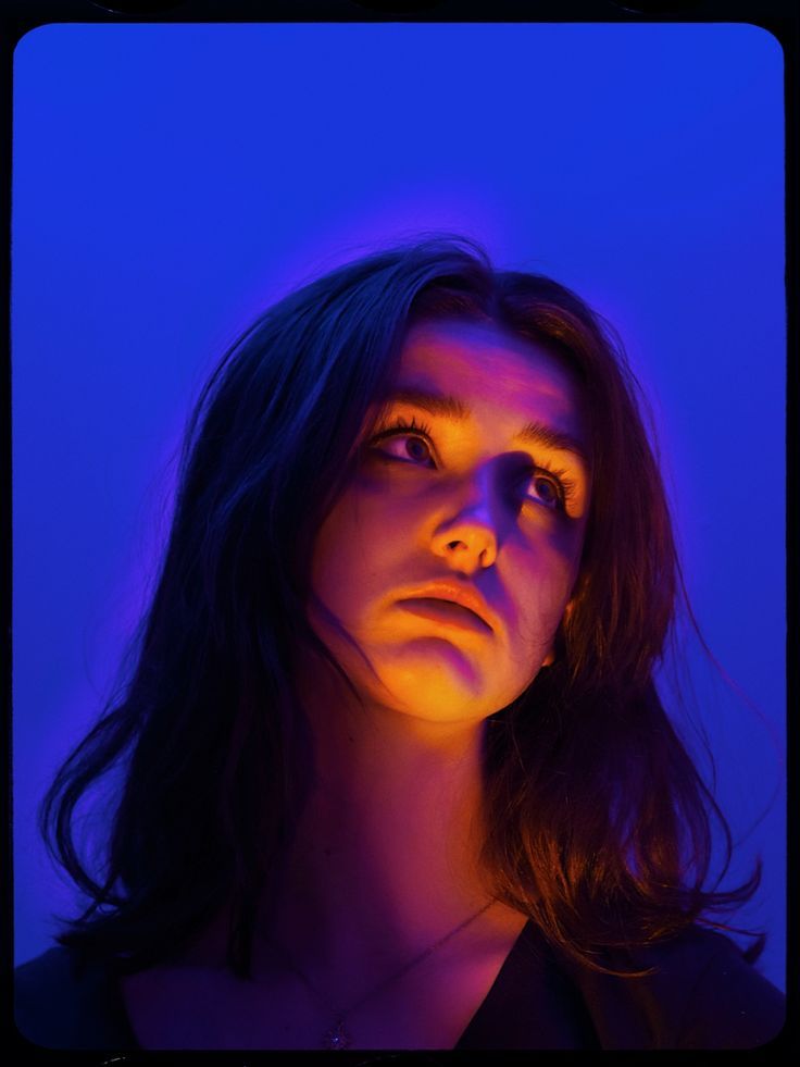 a woman with dark hair and blue lighting on her face is looking at the camera