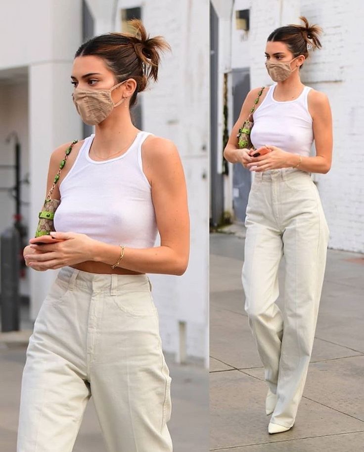 a woman in white shirt and pants walking down street with face mask covering her mouth