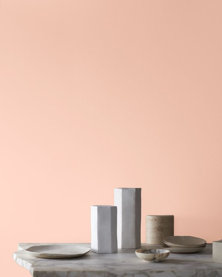 a table with plates, cups and vases sitting on top of it in front of a pink wall