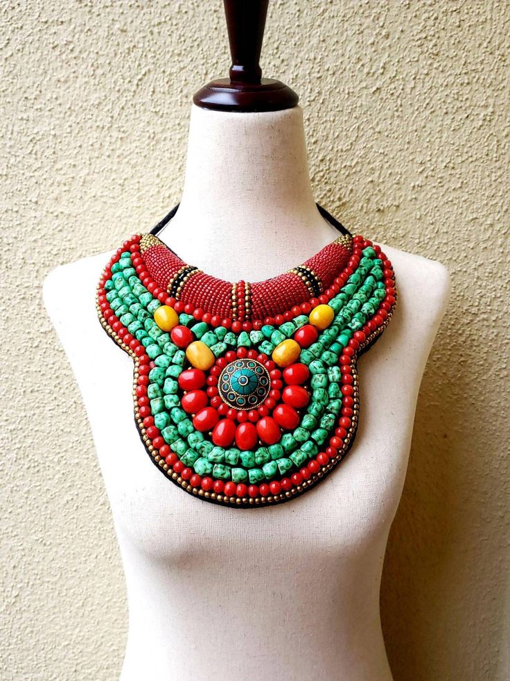 "Striking Tibetan turquoise and coral bib collar necklace in faux teal green turquoise, coral and amber beads, with a stunning central brass medallion. Perfect with a flowing caftan or an itsy black bikini. Perfect anywhere you are barefoot! Wear your hair up, with a bright ribbon or turban, or wear it down! You don't need much else! Eye-catching geometric pattern with a mix of smooth and textured beads. This is a handmade reproduction of a Tibetan tribal neck piece or Skeypuk, which is worn as Bohemian Turquoise Bib Necklace With Colorful Beads, Handmade Turquoise Bohemian Bib Necklace, Red Bohemian Bib Necklace For Festivals, Bohemian Red Bib Necklace With Round Beads, Green Bohemian Beaded Necklaces, Red Beaded Bohemian Bib Necklaces, Bohemian Bib Necklace With Colorful Beads, Green Turquoise Necklace With Colorful Beads For Festivals, Bohemian Beaded Necklaces With Round Beads