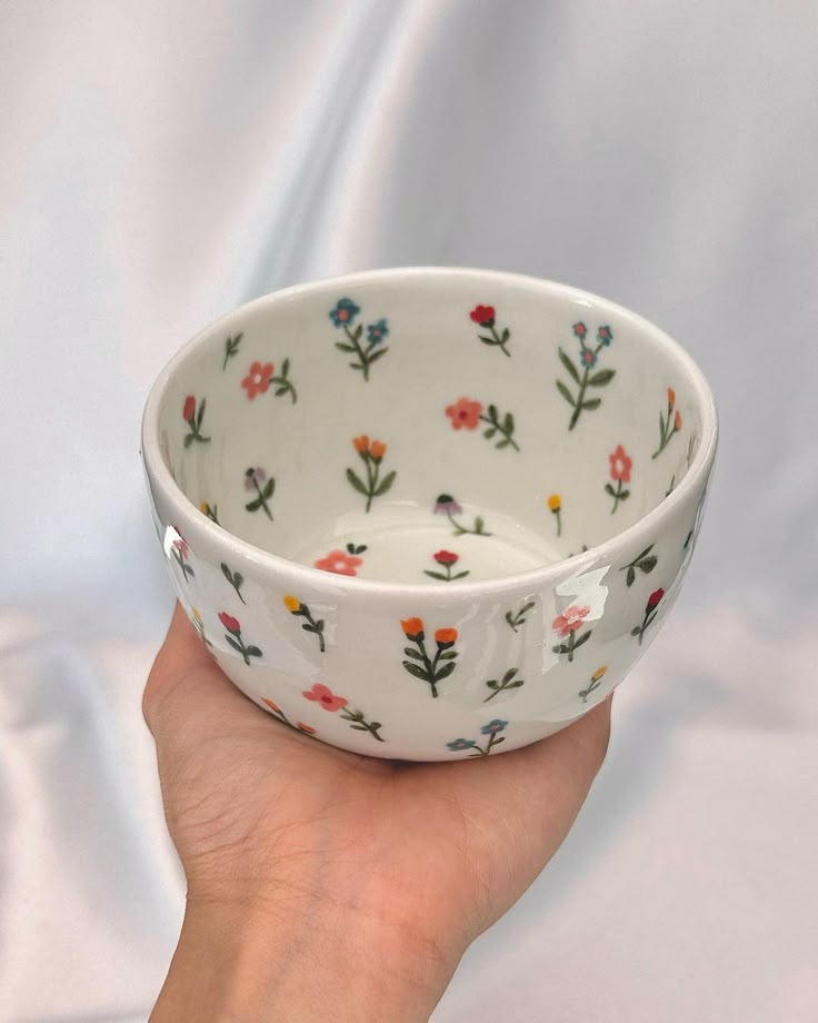 a hand holding a white bowl with flowers on it