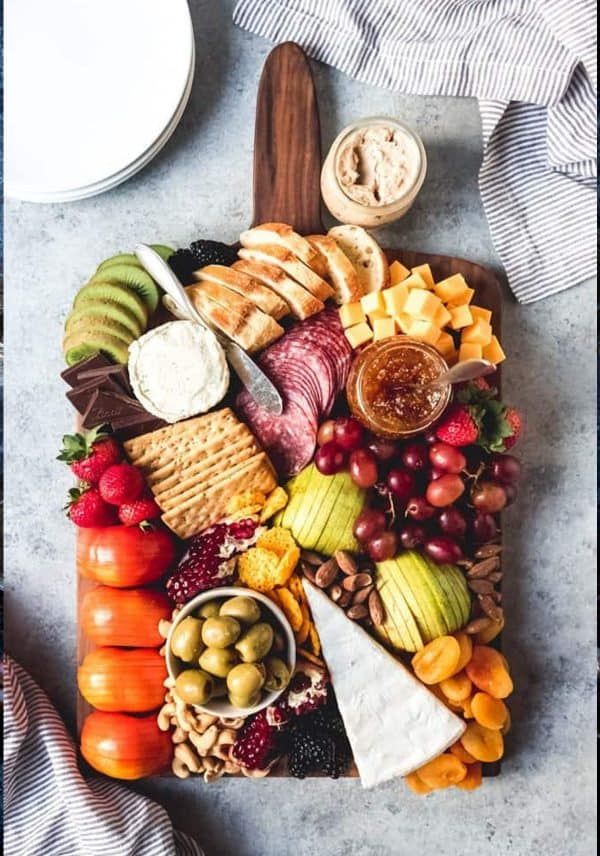 an assortment of cheeses, crackers and fruits on a platter with other food