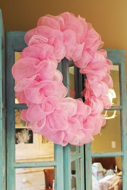 a pink wreath hanging from the side of a blue door in front of a mirror