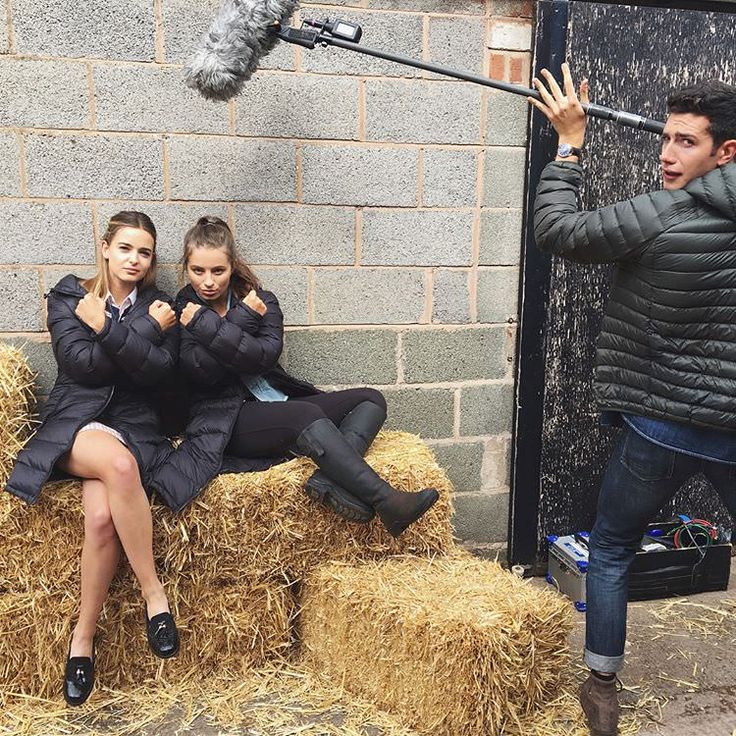 three people are sitting on hay and one person is holding an umbrella