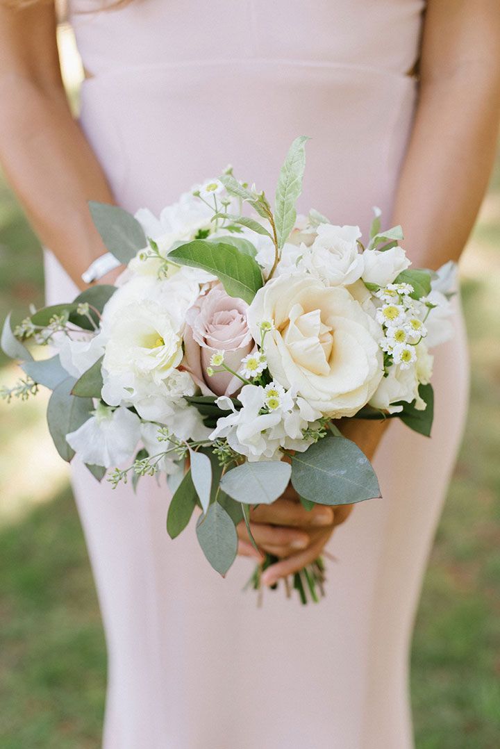 a bride holding a bouquet of white and pink flowers with greenery in her hands