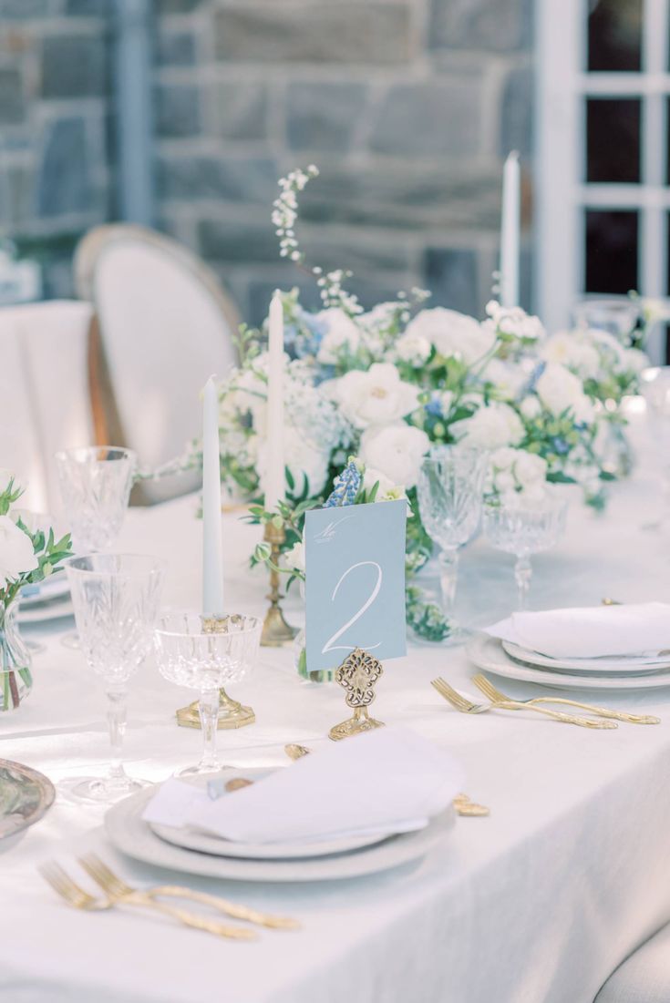 the table is set with white flowers and place settings