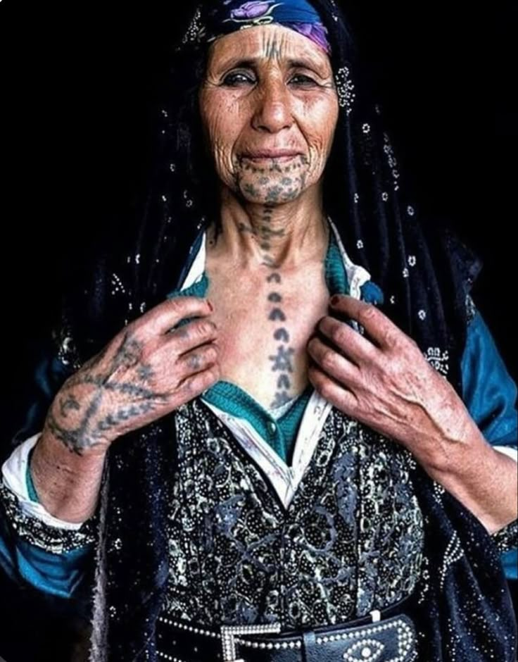 an old woman with tattoos on her chest and hands holding something in front of her face