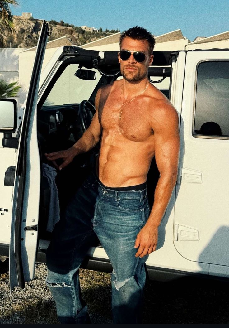 a shirtless man standing in the open door of a truck with his jeans on