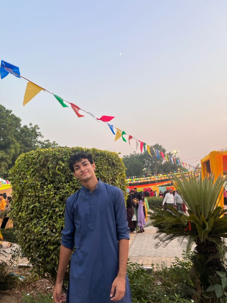 a man standing in front of some colorful flags and plants on a sunny day at an amusement park