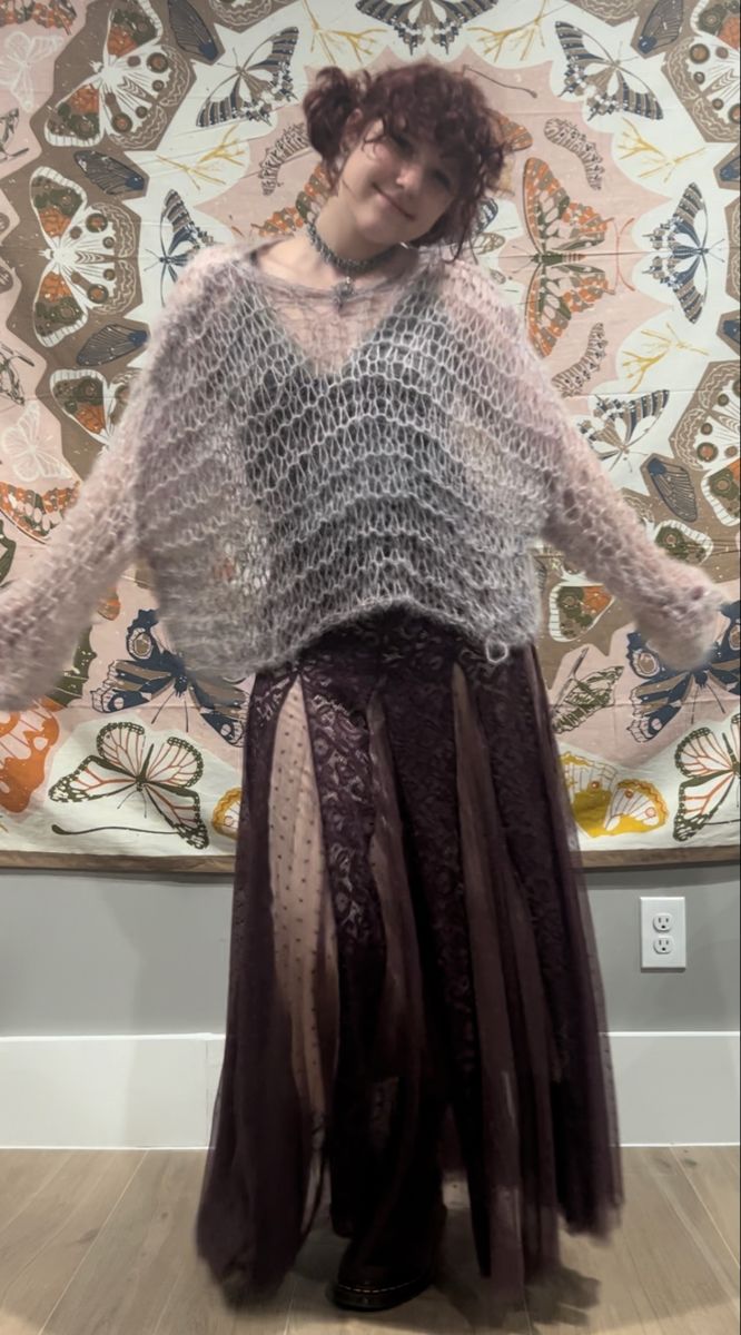 a woman standing in front of a painting wearing a long skirt and knitted sweater