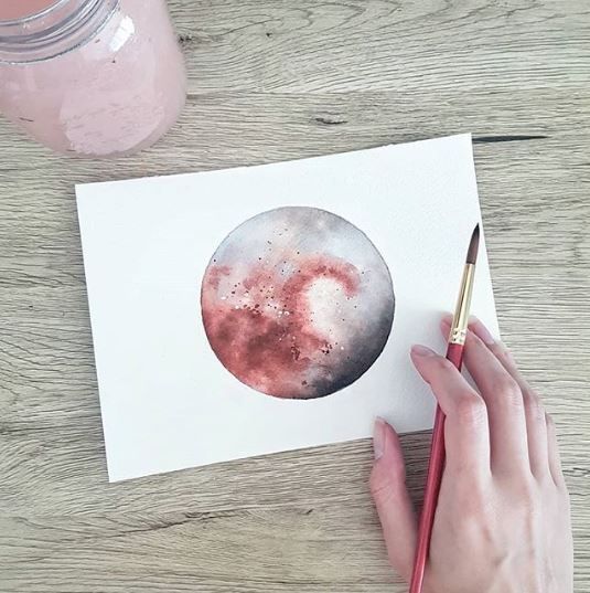 a person holding a paintbrush and drawing on paper with watercolors in front of them