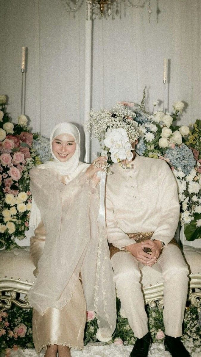 a man and woman sitting next to each other in front of flower covered wall with chandeliers