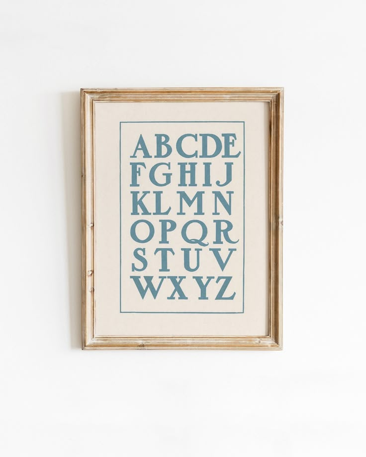 a cross stitch alphabet is hung on the wall in front of a white wall with a wooden frame