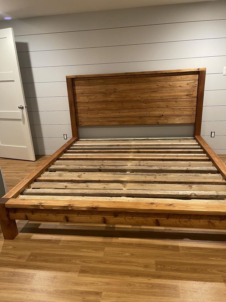 a bed frame made out of wood in a room with hard wood floors and white walls