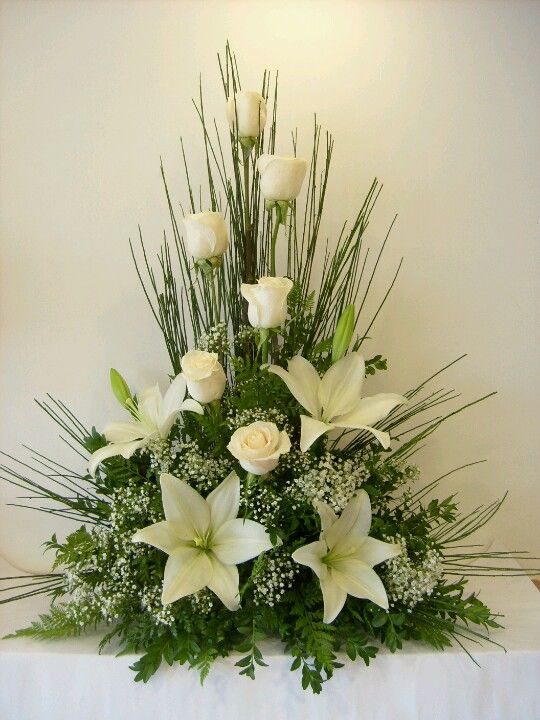 white flowers and greenery are arranged in a centerpiece on a tableclothed cloth