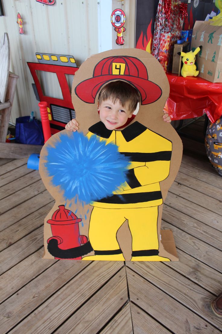 a young boy dressed up as a fireman holding a blue pom pom