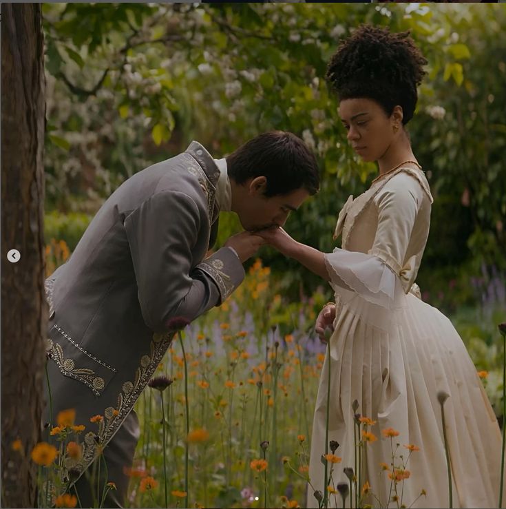 a man and woman standing next to each other in a flower filled field with trees