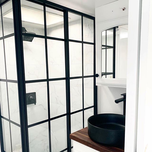 a bathroom with black and white tile on the walls, shower stall door and sink