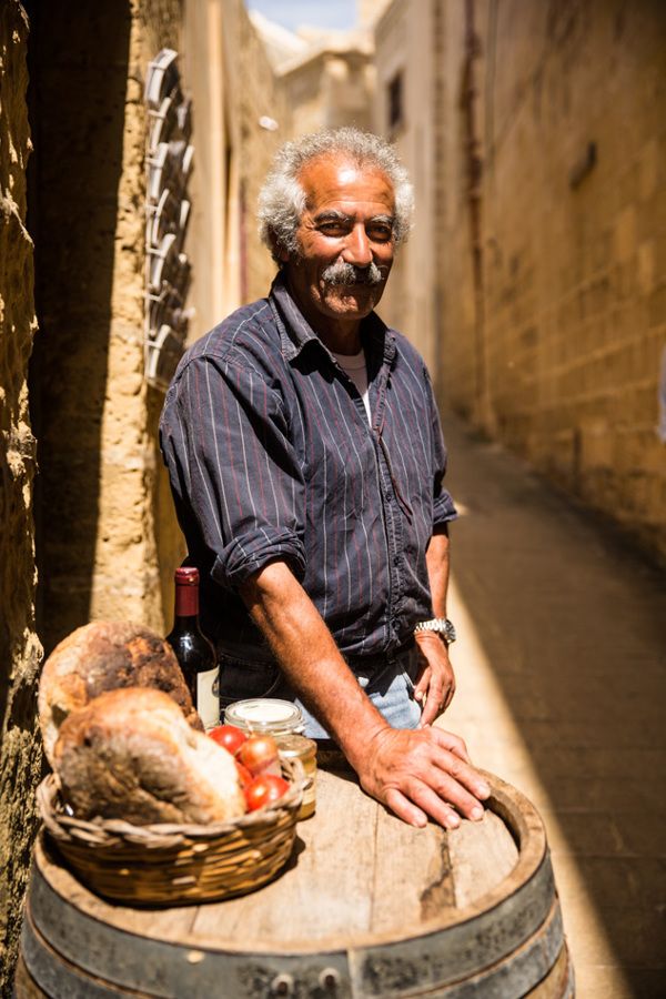 a man sitting on top of a barrel next to a basket filled with bread and wine