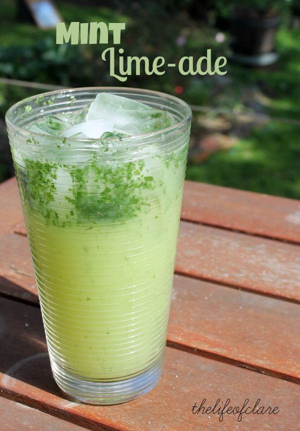 a glass filled with green liquid sitting on top of a wooden table next to trees