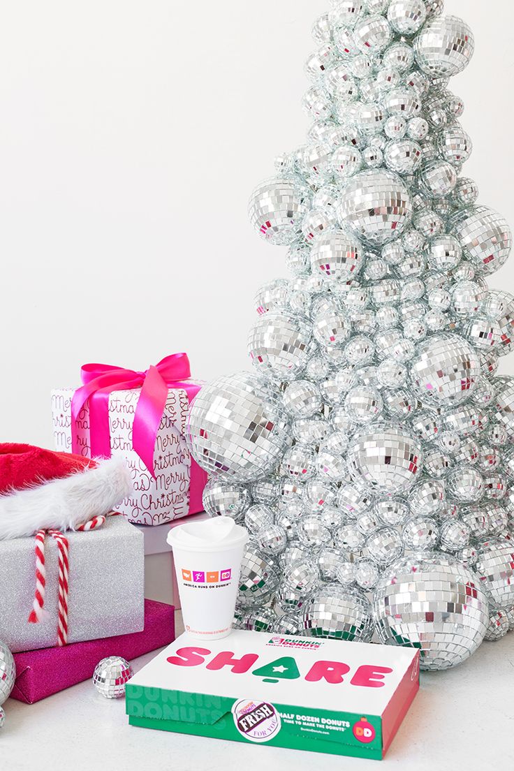 a white christmas tree with shiny silver balls and presents under it, next to a santa hat