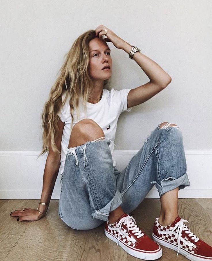 a woman sitting on the floor with her legs crossed and wearing red converse shoes,