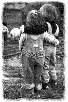 two young children standing next to each other on top of a grass covered field with sheep in the background