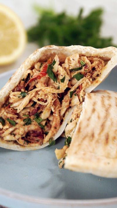 a pita sandwich with chicken and vegetables on a blue plate next to lemon wedges