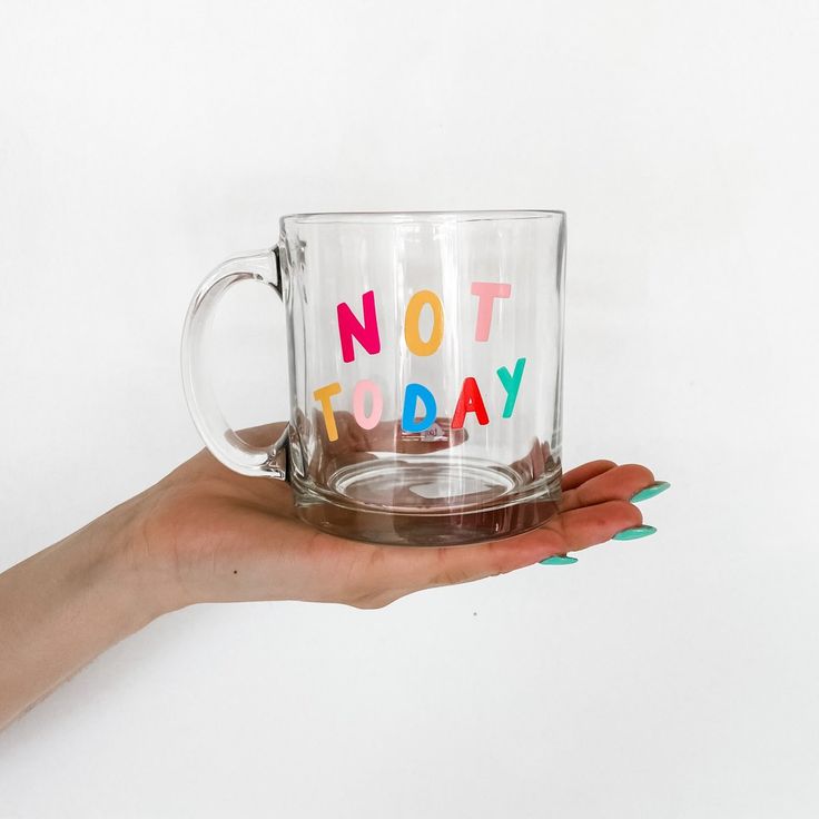 a person holding a glass mug with the words not today written on it in multicolored letters