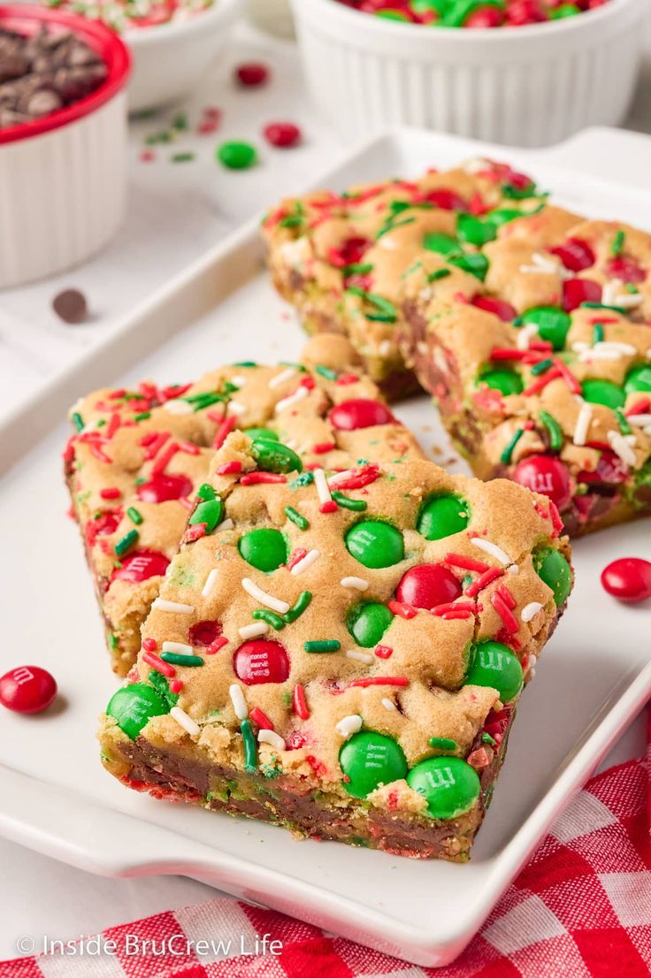 three pieces of christmas cookie bars on a white plate with candy and sprinkles