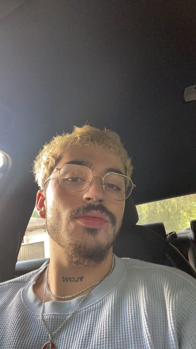 a man with glasses sitting in the back seat of a car, looking at the camera