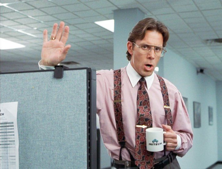 a man with glasses and suspenders is holding his hand up in the air while standing next to an office cubicle