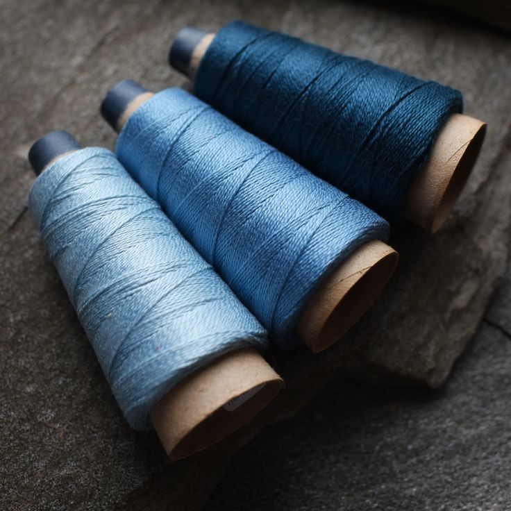 three spools of blue thread sitting on top of a piece of wood next to each other