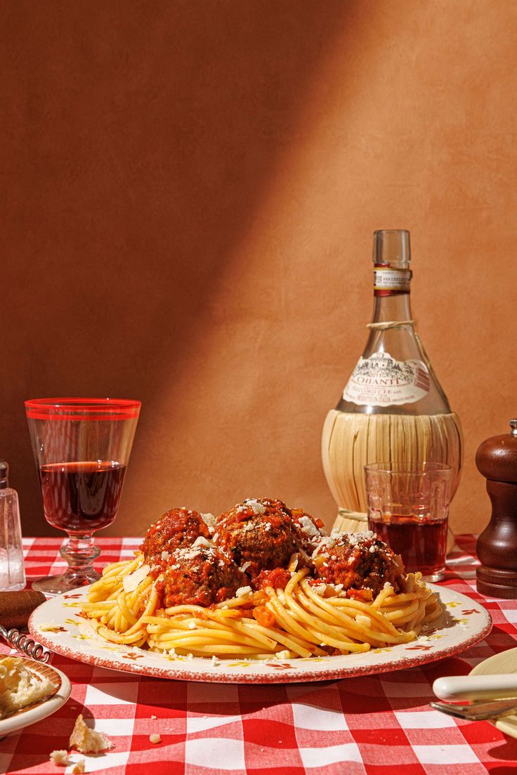 a plate of spaghetti with sauce and bread on a tablecloth next to wine bottles