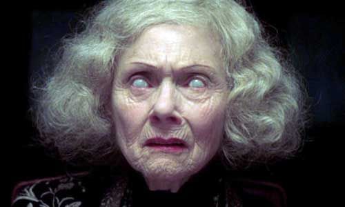 an older woman with blonde hair and blue eyes stares at the camera in a dark room