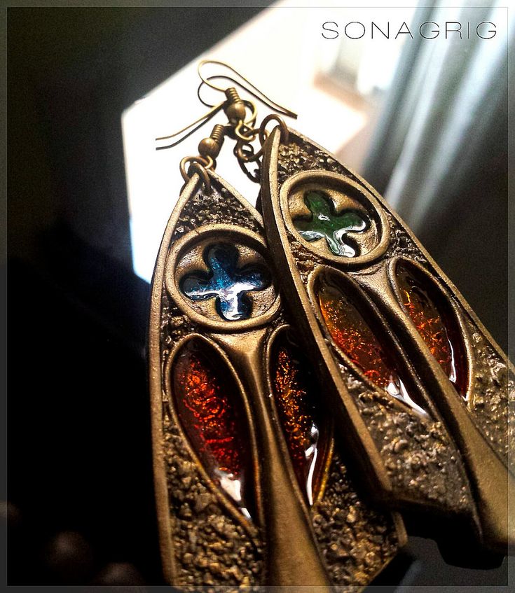 two pairs of gold colored metal earrings hanging from hooks on a window sill in the sunlight