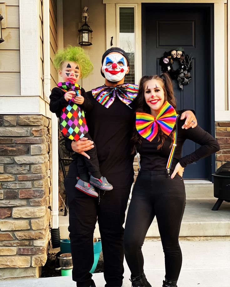 three people dressed up as clowns pose in front of a house for a photo