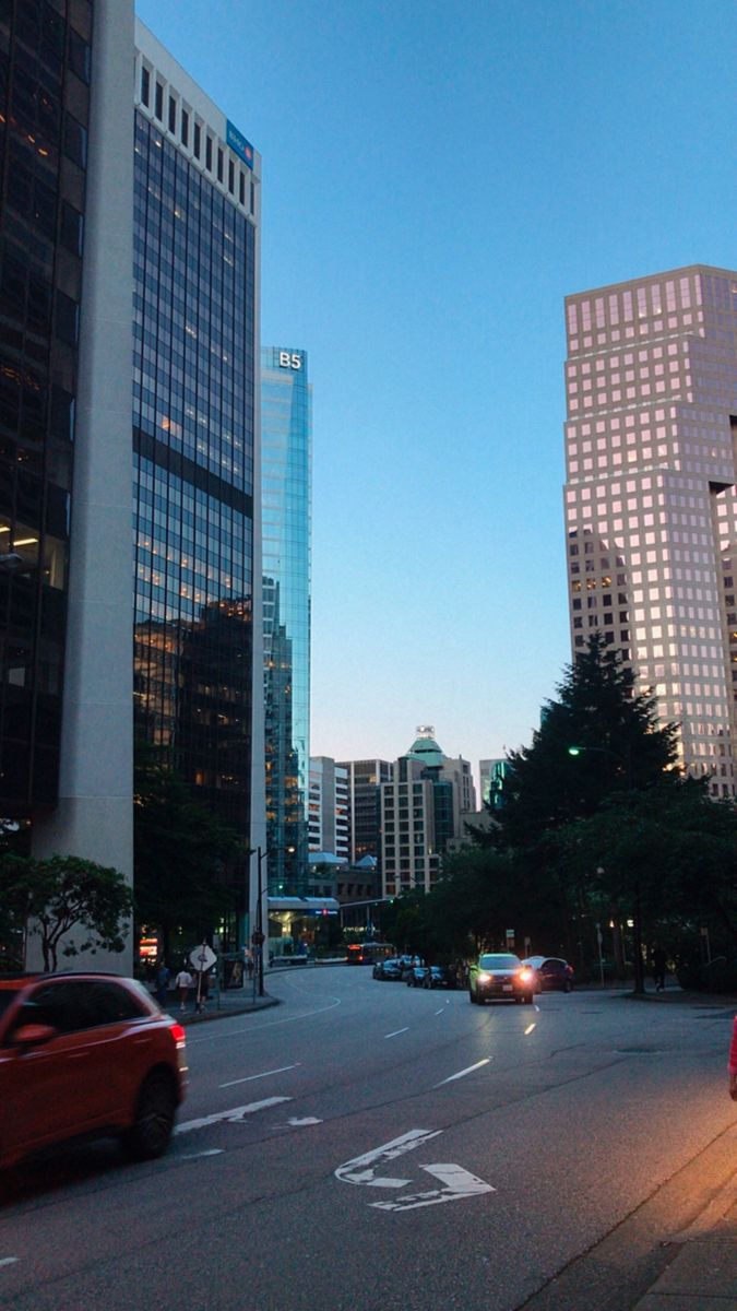 cars are driving down the street in front of tall buildings and skyscrapers at dusk