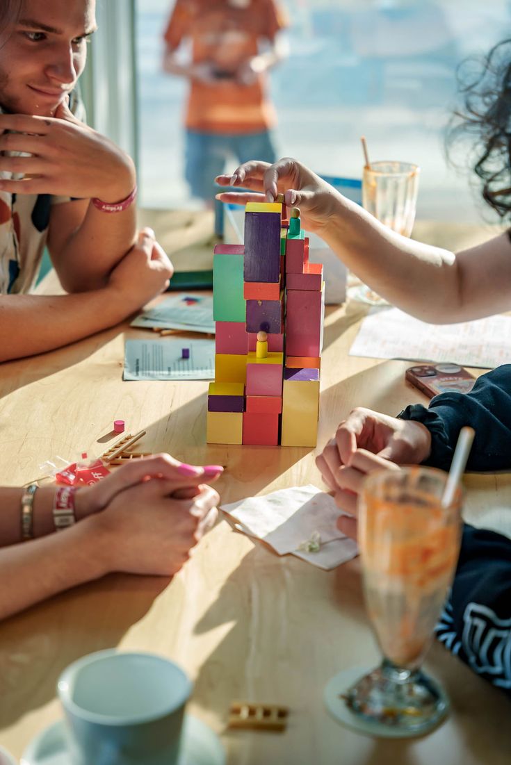 several people sitting around a table playing with wooden blocks and building them into a tower