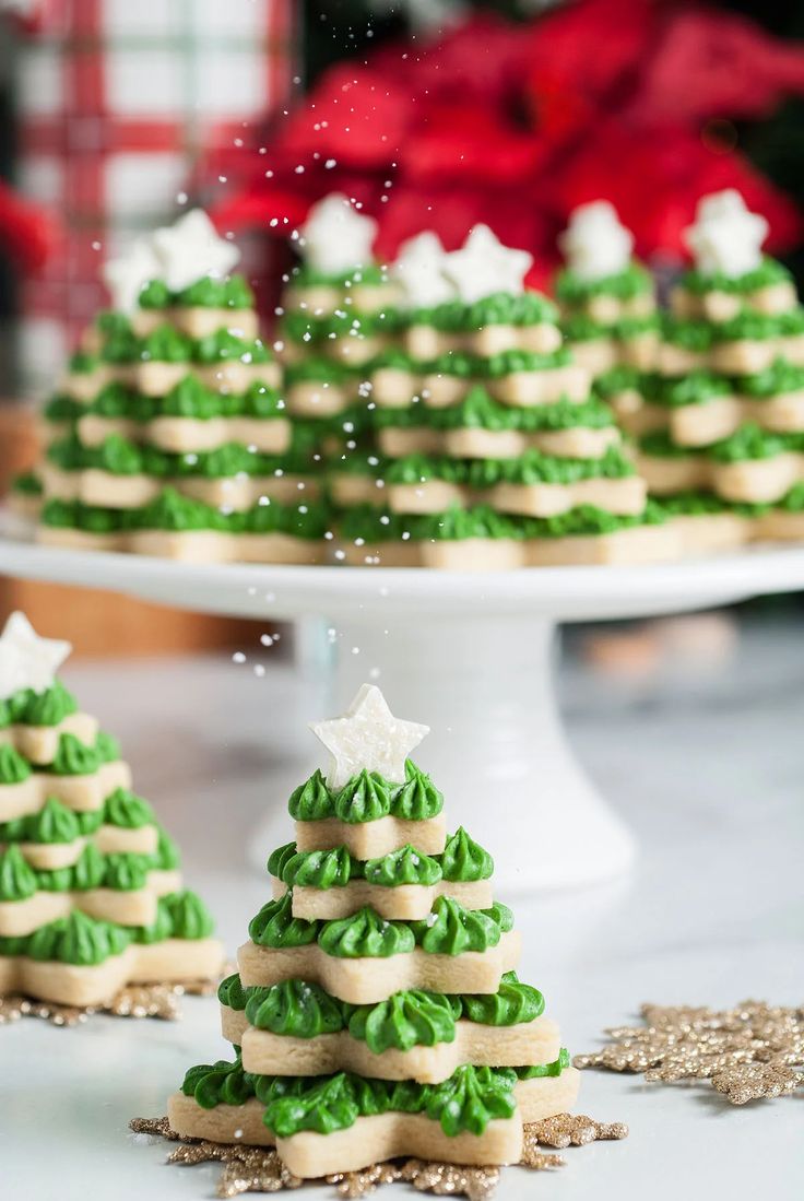 green and white decorated cookies sitting on top of a cake plate next to a christmas tree