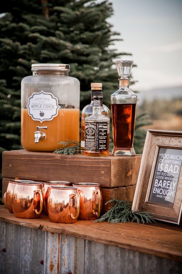 an assortment of alcohol bottles and glasses sitting on top of a wooden box next to a pine tree