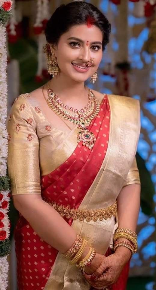 a woman in a red and white sari with gold jewelry on her neck, posing for