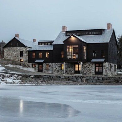 a large black house sitting on top of a snow covered hill next to a lake